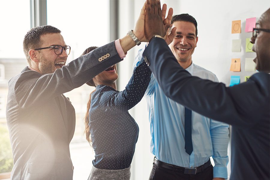 Business Insurance - Group of Colleagues at a Business Meeting in the Office Giving Each Other High Fives to Celebrate Success