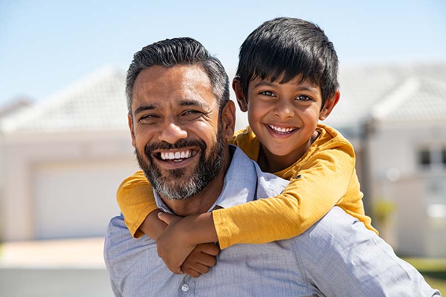 Insurance Quote - Closeup View of Smiling Father Giving His Son a Piggyback Ride Outside in Front of Their House