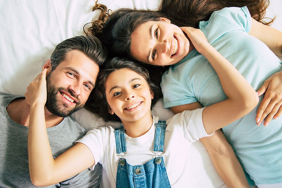 Personal Insurance - Closeup View of Joyful Parents Laying in Bed with Their Smiling Daughter